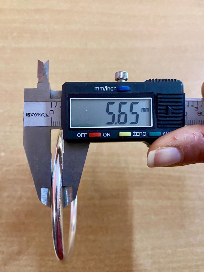 May include: A silver bangle bracelet being measured with a digital caliper. The caliper reads 5.65 mm.