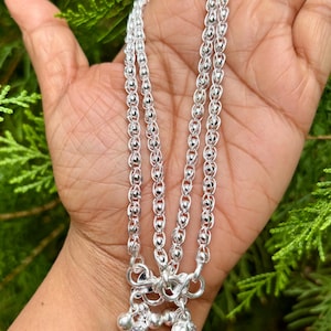 May include: A pair of silver anklets with a beaded chain design and a dangling charm with a clear crystal. The anklets are shown on a hand against a green background.