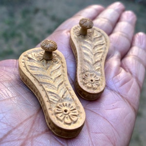Pu&ograve; includere: Due piccoli porta incenso in legno intagliati in modo intricato a forma di sandali. I porta incenso sono di colore marrone chiaro e hanno un motivo floreale.