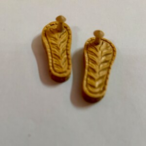 May include: Two wooden sandals with a carved design. The sandals are light brown and have a small wooden peg on the back.