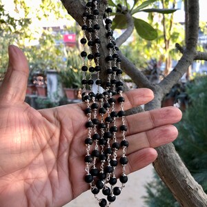 May include: A black beaded necklace with a silver chain. The necklace is made of round beads and has a silver clasp.
