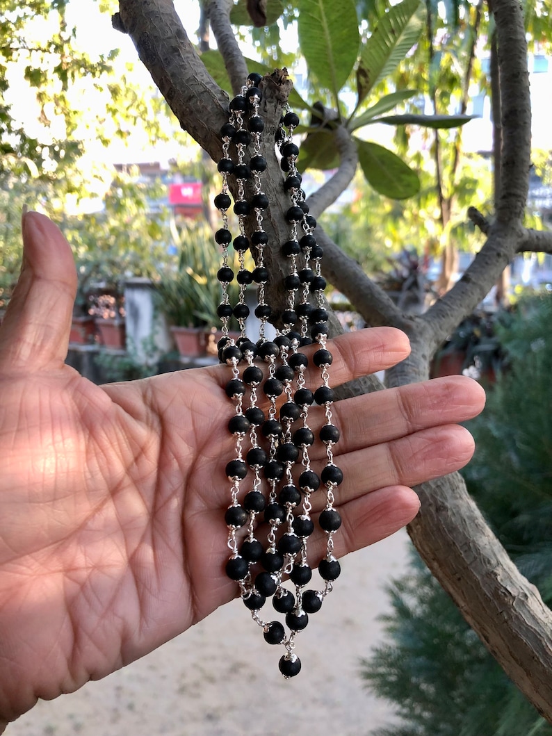 May include: A black beaded necklace with a silver chain. The necklace is made of round beads and has a silver clasp.