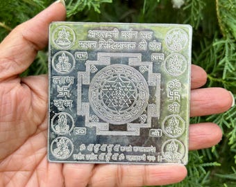 Puede incluir: Un yantra cuadrado de plata con un diseño Sri Yantra en el centro. El yantra está rodeado de ocho imágenes más pequeñas de Lakshmi, la diosa hindú de la riqueza. El yantra está inscrito con texto sánscrito, incluidas las palabras "Astalakshmi Darshan Sah" y "Maha Siddhi Dayak Sri Yantra".