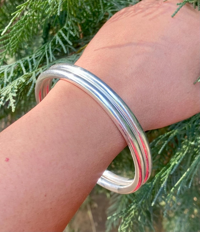May include: A silver bangle bracelet with a wide, rounded design. The bracelet is made of two thick bands of silver that are joined together.