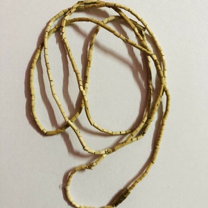 May include: A long strand of light brown beads made of small, rectangular pieces. The beads are strung together to form a necklace.