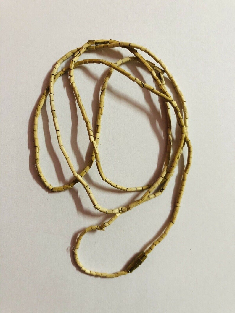 May include: A long strand of light brown beads made of small, rectangular pieces. The beads are strung together to form a necklace.