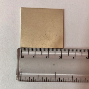 May include: A gold-colored metal sheet measuring approximately 3 inches by 3 inches.