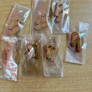 May include: Multiple pairs of brown flip-flop sandals are packaged in clear plastic bags. The sandals have a woven design.