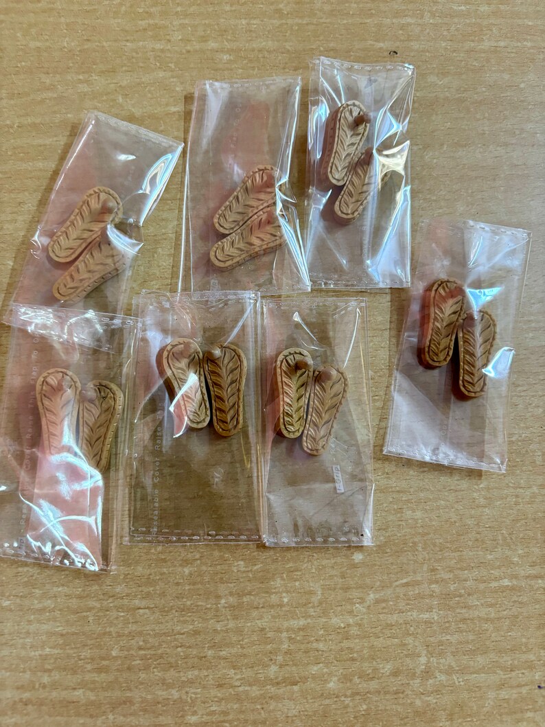 May include: Multiple pairs of brown flip-flop sandals are packaged in clear plastic bags. The sandals have a woven design.