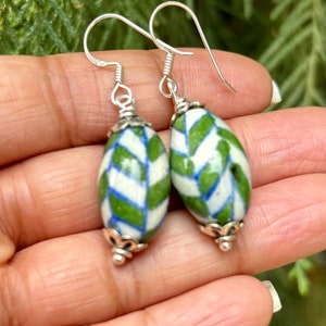 May include: A pair of silver dangle earrings with green and white ceramic beads. The beads have a geometric pattern.