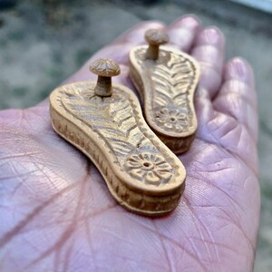 Pu&ograve; includere: Due piccoli porta incenso in legno intagliati in modo intricato a forma di sandali. I porta incenso sono di colore marrone chiaro e hanno un design floreale.
