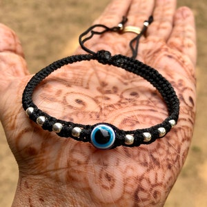 May include: Black string bracelet with silver beads and a blue evil eye charm.