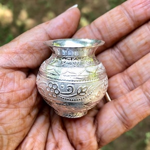 Könnte beinhalten: Eine kleine silberne Vase mit aufwendigen floralen Mustern. Die Vase ist etwa 5 cm hoch und hat einen runden Körper mit einem schmalen Hals.