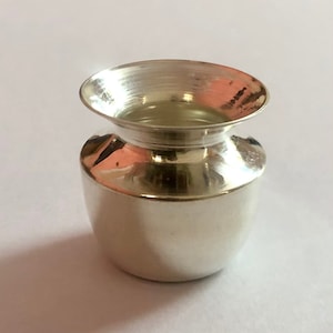 Może przedstawiać: Mały, srebrny, ozdobny dzbanek z zaokrąglonym korpusem i szerokim, rozszerzającym się otworem. Dzbanek jest wypolerowany i błyszczący.