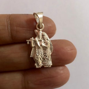 Op de afbeelding: Zilveren hanger met een gedetailleerde afbeelding van Radha Krishna, een hindoe&iuml;stisch godenpaar, in een liefdevolle omhelzing. De hanger is ontworpen met ingewikkelde details en een traditionele stijl.