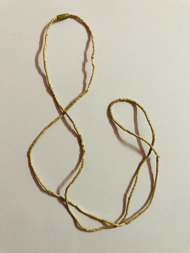 May include: A long, thin necklace made of small, light brown beads. The necklace is made of two strands of beads that are connected by a small, gold clasp.