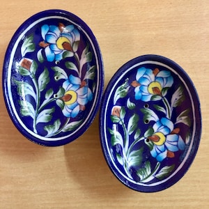 Könnte beinhalten: Zwei ovale Seifenschalen aus Keramik. Sie sind tiefblau mit weißem Rand und einem Blumendesign in Blau, Gelb und Grün. Jede Schale hat drei Abflusslöcher. Das Design ist handbemalt.