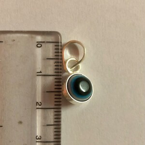 Puede incluir: Un amuleto de plata con un dise&ntilde;o de ojo turco azul y negro. El amuleto mide aproximadamente 2,5 cm de di&aacute;metro y tiene un bucle para sujetarlo a un collar o pulsera.