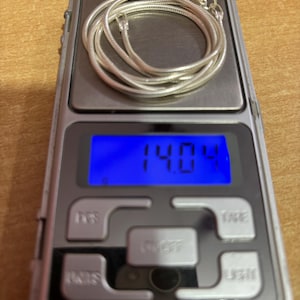 Puede incluir: Un collar de cadena de serpiente de plata en una b&aacute;scula digital que muestra un peso de 14,04 gramos.