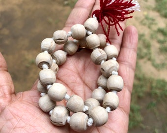 Könnte beinhalten: Eine weiße Holz-Mala-Kette mit einem roten und weißen Quasten. Die Kette besteht aus runden Perlen und ist mit weißem Garn aufgereiht.