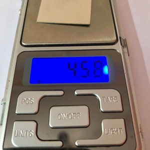 May include: A silver digital scale with a blue display showing 4.58 grams. The scale has buttons labeled "PCS", "TARE", "ON/OFF", "UNITS", and "LIGHT".
