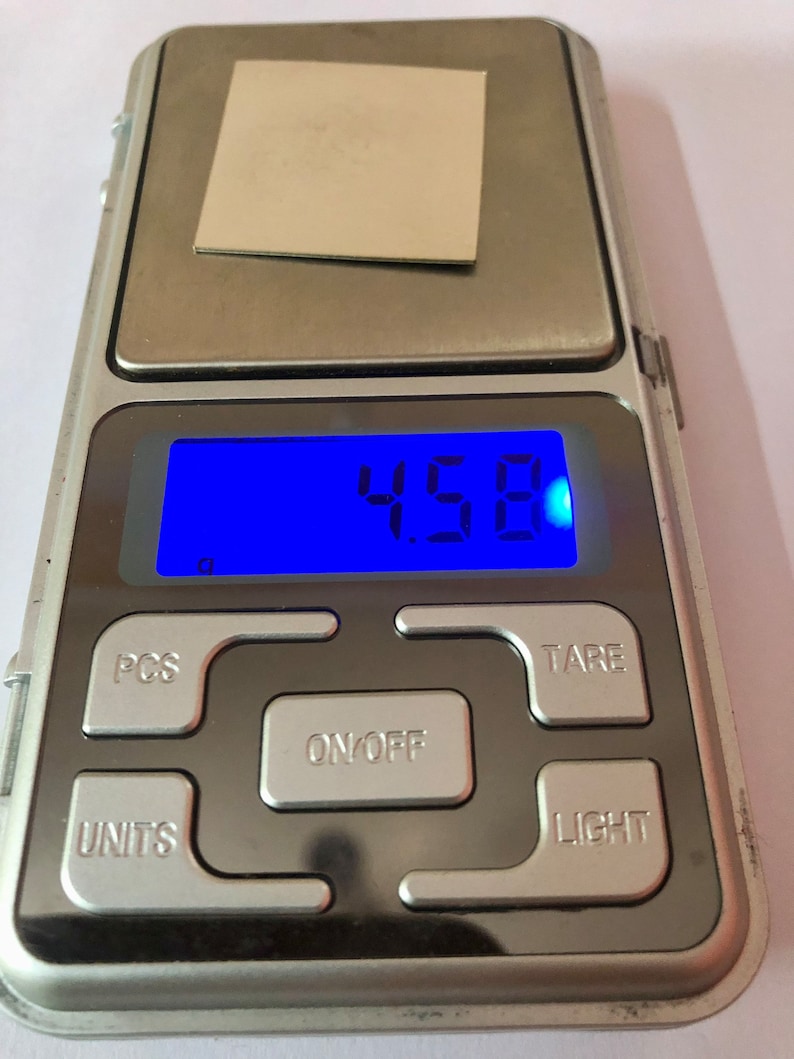 May include: A silver digital scale with a blue display showing 4.58 grams. The scale has buttons labeled "PCS", "TARE", "ON/OFF", "UNITS", and "LIGHT".