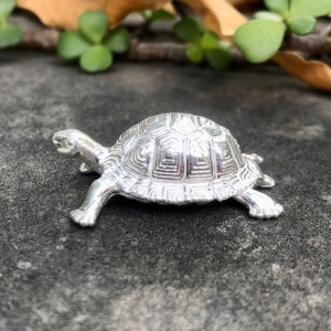Peut inclure: Une figurine de tortue en argent avec un motif de carapace détaillé. La tortue marche en avant, la tête levée.