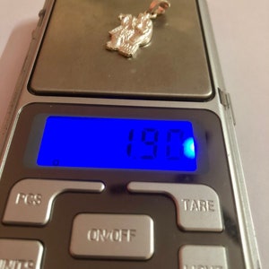 Op de afbeelding: Een zilveren hanger met een gewicht van 1,90 gram op een digitale weegschaal. De hanger heeft een gedetailleerd ontwerp van een religieuze figuur.