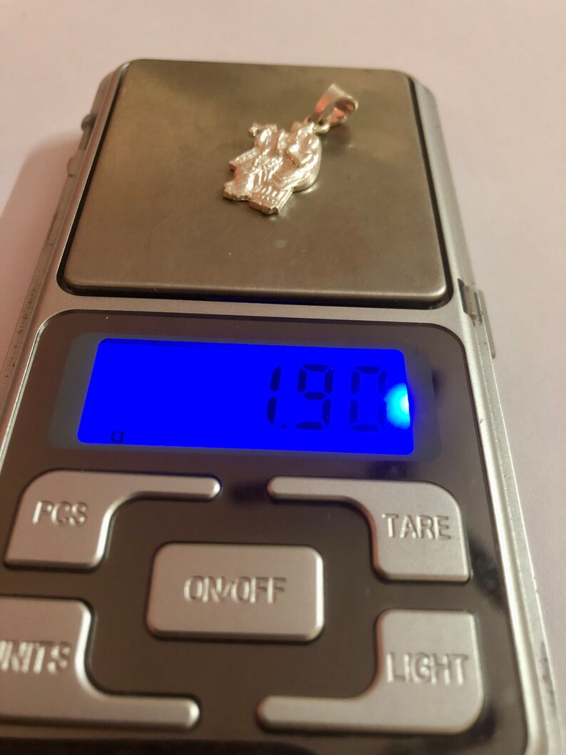 Op de afbeelding: Een zilveren hanger met een gewicht van 1,90 gram op een digitale weegschaal. De hanger heeft een gedetailleerd ontwerp van een religieuze figuur.
