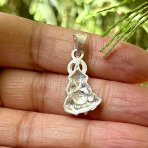 May include: A silver pendant featuring a detailed design of a woman in a dress. The pendant has a loop at the top for attaching to a chain.