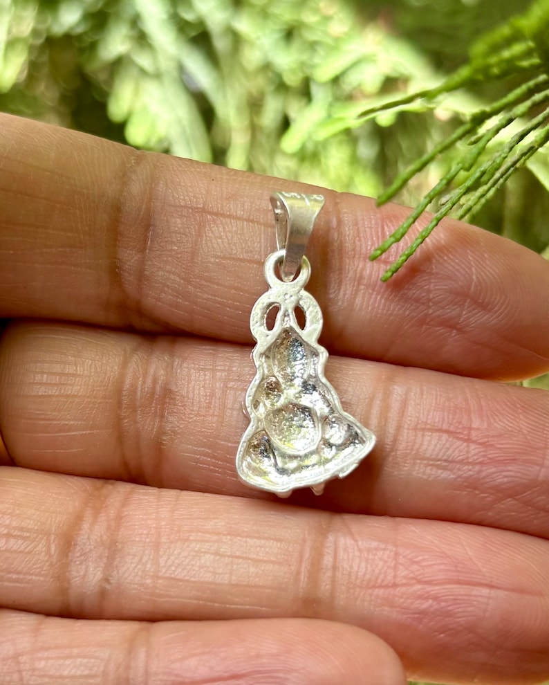 May include: A silver pendant featuring a detailed design of a woman in a dress. The pendant has a loop at the top for attaching to a chain.