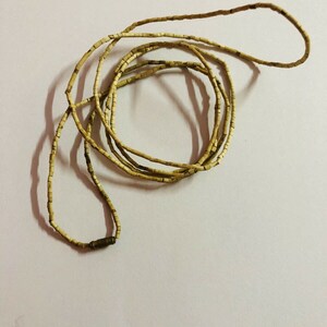 May include: A long strand of light brown beads made of natural materials. The beads are small and rectangular, and the strand is coiled into a circle.