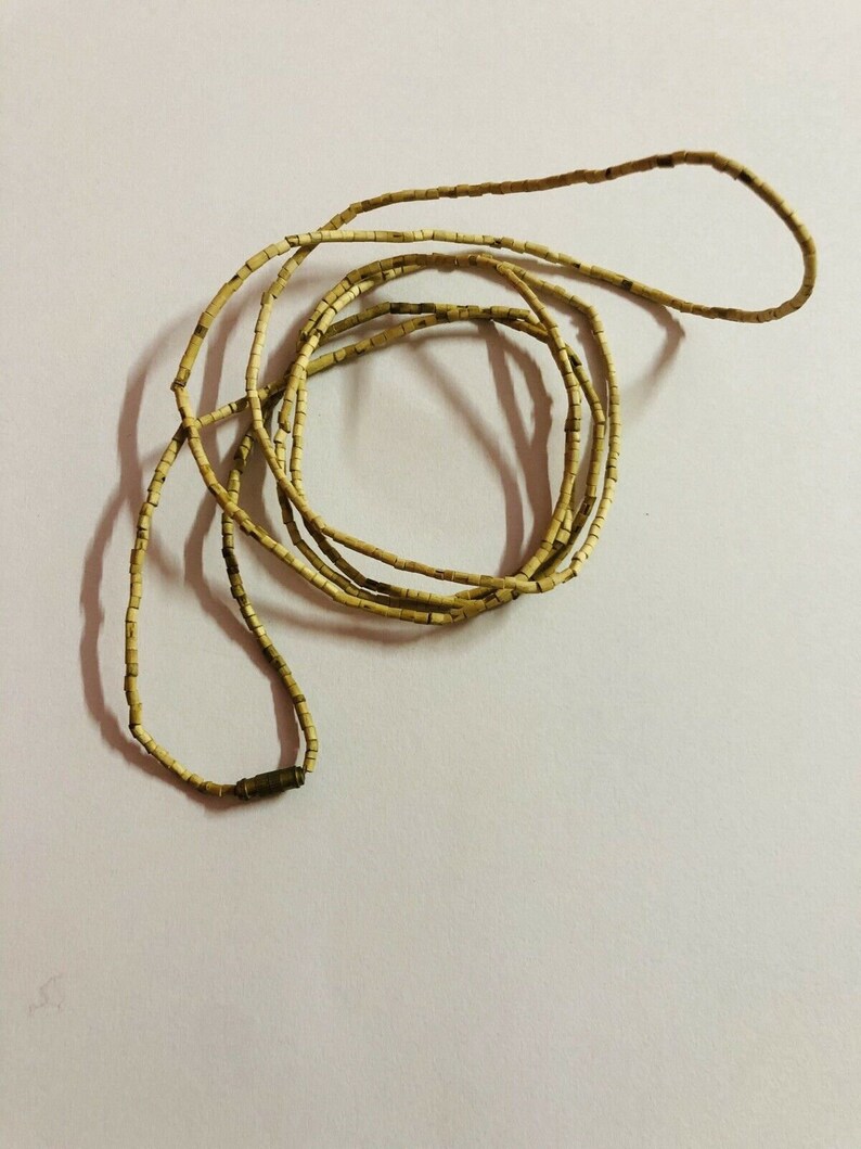 May include: A long strand of light brown beads made of natural materials. The beads are small and rectangular, and the strand is coiled into a circle.