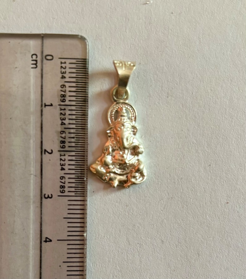 May include: Silver pendant featuring a detailed depiction of the Hindu deity Ganesha. The pendant is approximately 2 cm in height and is ready to be added to a necklace or chain.