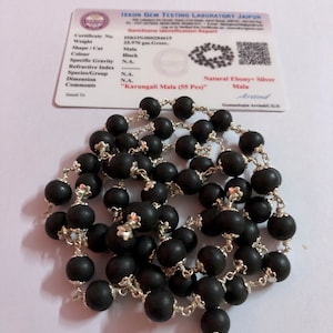 Puede incluir: Un collar Mala Karungali negro con 55 cuentas, cada una conectada por metal color plata. El collar se muestra con un informe de identificación de piedras preciosas de ISKON GEM TESTING LABORATORY JAIPUR.