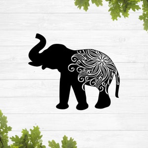 Puede incluir: Silueta negra de un elefante con un diseño de mandala blanco en su costado. El elefante está de pie sobre un fondo de madera blanca.
