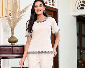 Puede incluir: Un conjunto de pijama de dos piezas de color beige. La parte superior tiene mangas cortas y cuello redondo, con ribete en blanco y negro. Los pantalones cortos a juego completan el conjunto. La modelo lleva tacones transparentes. El conjunto es de un material suave y cómodo.