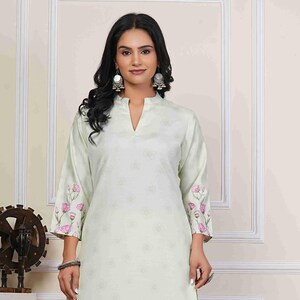 May include: A light green floral print kurta and matching pants set. The kurta features a V-neck and three-quarter sleeves with pink floral accents. The floral pattern continues along the bottom of the kurta. The pants are a solid light green color.