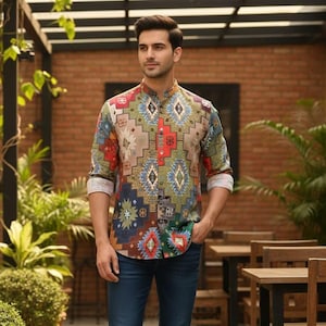 Puede incluir: Un hombre con una camisa de manga larga estampada con cuello mandarín y vaqueros azul oscuro. La camisa presenta un diseño geométrico colorido en tonos marrón, rojo, azul y verde. Lleva mocasines de cuero marrón.