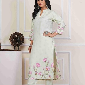 May include: A light green floral print kurta and matching pants set. The kurta features a mandarin collar and three-quarter sleeves with pink floral accents. The pants are a solid light green color. The outfit is worn with clear heeled sandals.