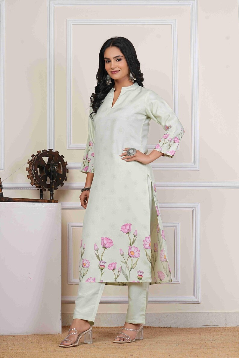 May include: A light green floral print kurta and matching pants set. The kurta features a mandarin collar and three-quarter sleeves with pink floral accents. The pants are a solid light green color. The outfit is worn with clear heeled sandals.