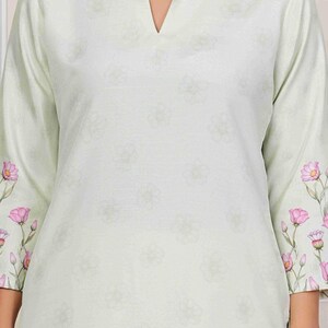 May include: A light green tunic with a V-neck and three-quarter sleeves. The sleeves are adorned with pink floral patterns. The tunic has a subtle floral pattern throughout.