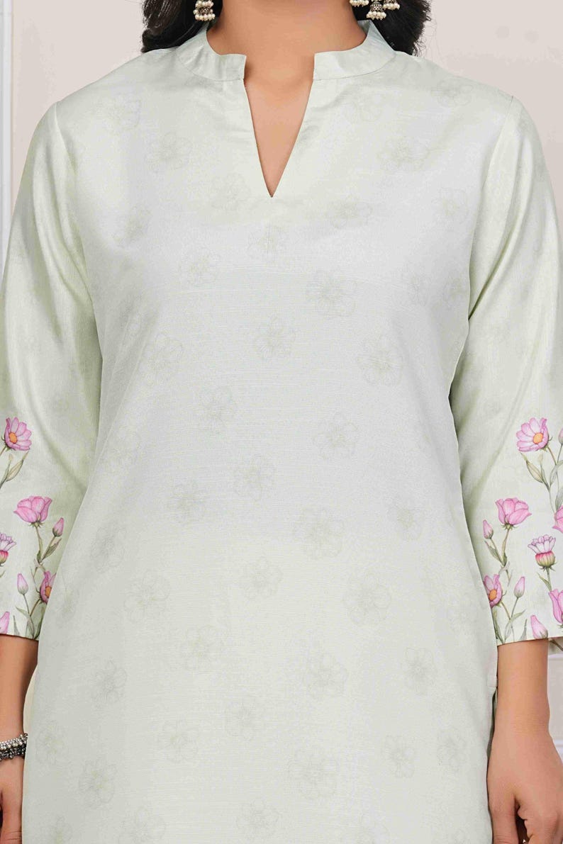 May include: A light green tunic with a V-neck and three-quarter sleeves. The sleeves are adorned with pink floral patterns. The tunic has a subtle floral pattern throughout.