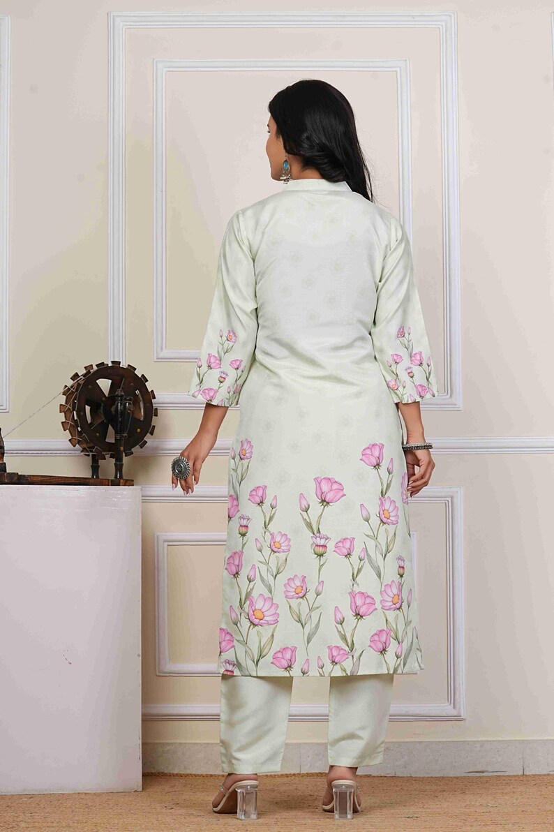 May include: A light green floral print kurta and matching pants set. The long-sleeved kurta features a high collar and is adorned with pink flower designs. The pants are a solid light green color. The outfit is suitable for casual or semi-formal occasions.