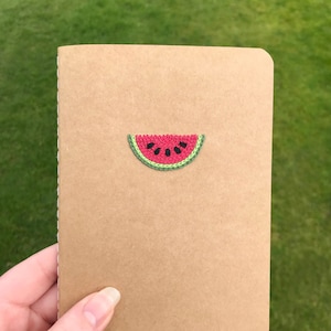 Puede incluir: Una libreta marrón con una sandía bordada en la parte delantera.