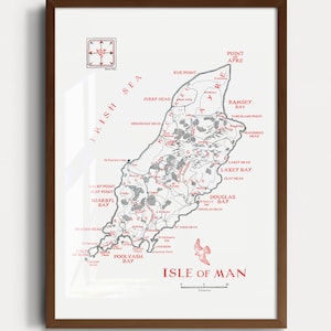Puede incluir: Impresión enmarcada del mapa de la Isla de Man, con una ilustración detallada en blanco y negro con detalles en rojo. El mapa incluye características geográficas y nombres de lugares, con el título "Isle of Man" en la parte inferior. El marco es de color marrón oscuro.