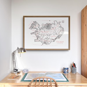 May include: A framed wall art print featuring a detailed black and white map of Iceland with red text labels, including the word &Iacute;SLAND. The map is displayed in a light brown wooden frame, showcasing geographical features and coastlines.