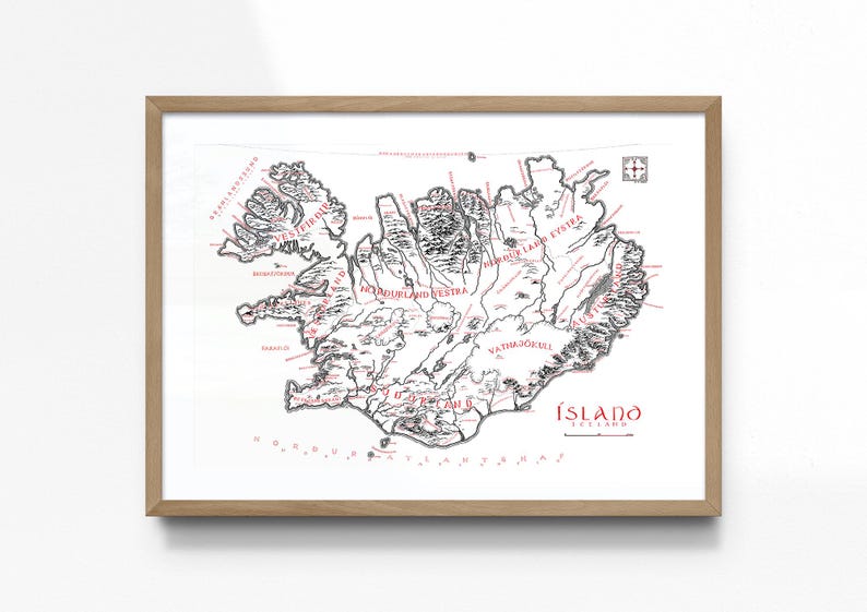 May include: A framed map of Iceland featuring black ink topography and red text labels. The map displays regional names, a compass rose in the top right corner, and the title &Iacute;SLAND ICELAND in the bottom right, all encased in a light wood frame.