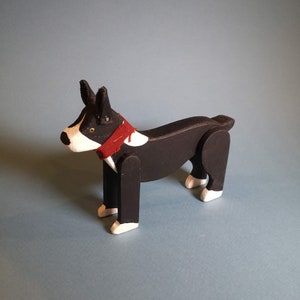 Pu&ograve; includere: Un cane di legno nero e bianco con un collare rosso. Il cane &egrave; in piedi su una superficie blu chiaro.