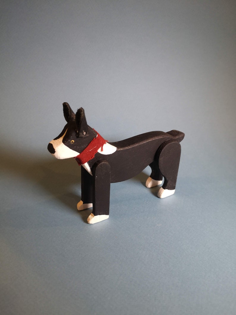 Pu&ograve; includere: Un cane di legno nero e bianco con un collare rosso. Il cane &egrave; in piedi su una superficie blu chiaro.